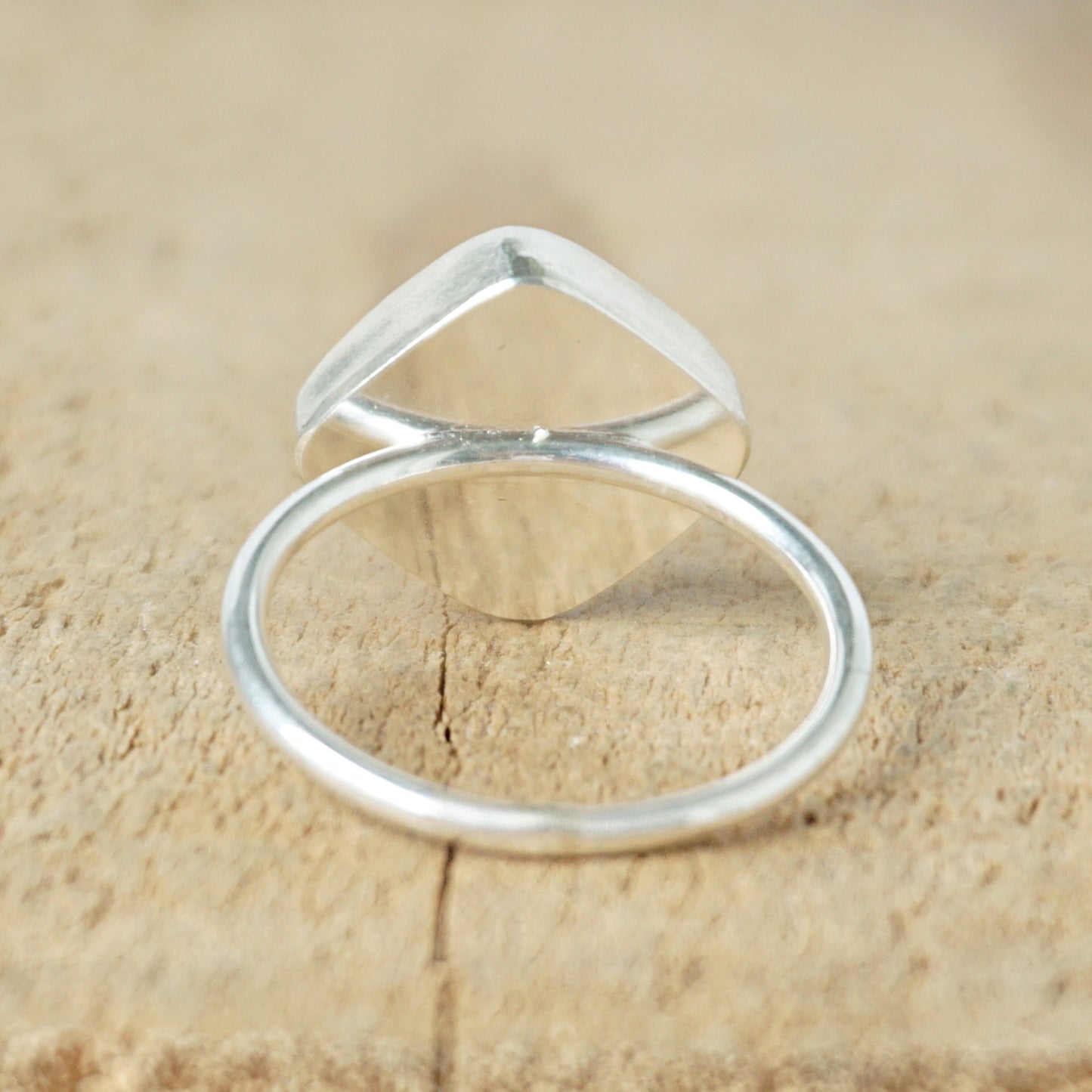 back view of a silver ring with a striped stone on a wooden background