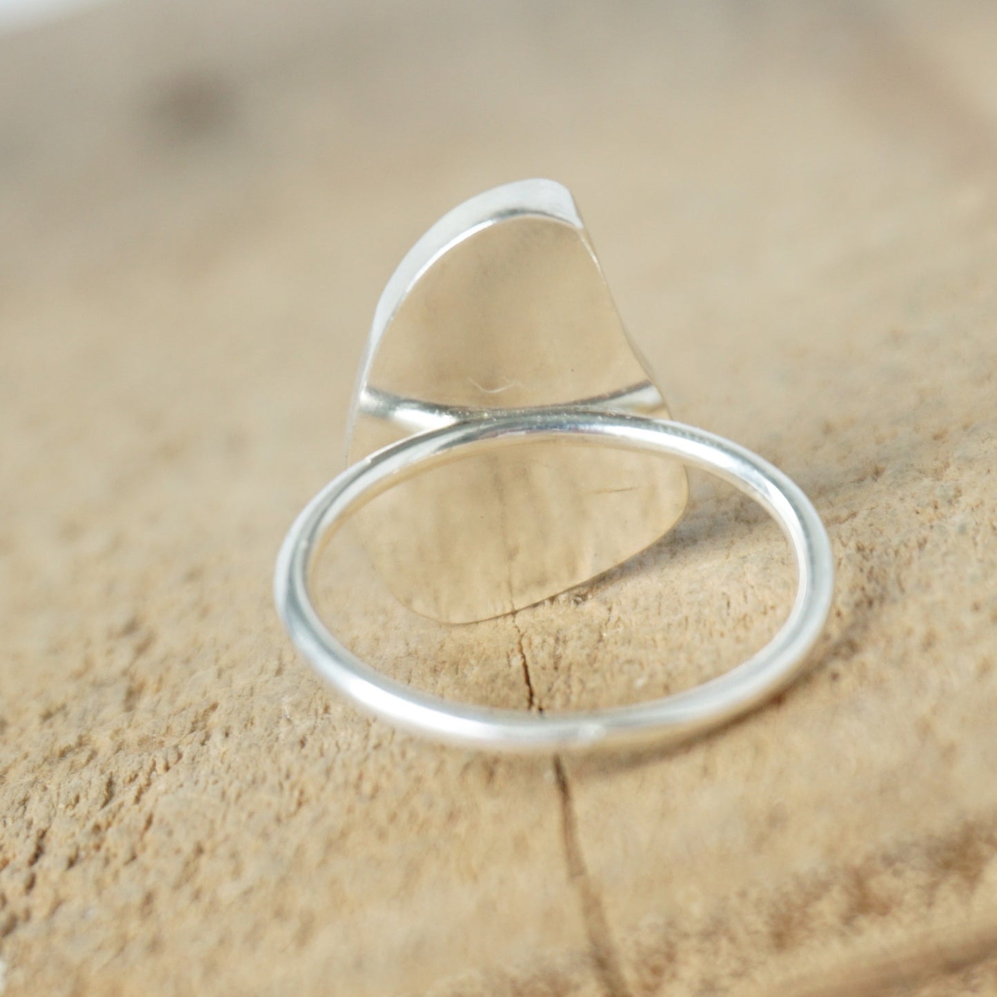 back view of a light aqua blue sea glass ring with a sterling silver setting, against a wooden background