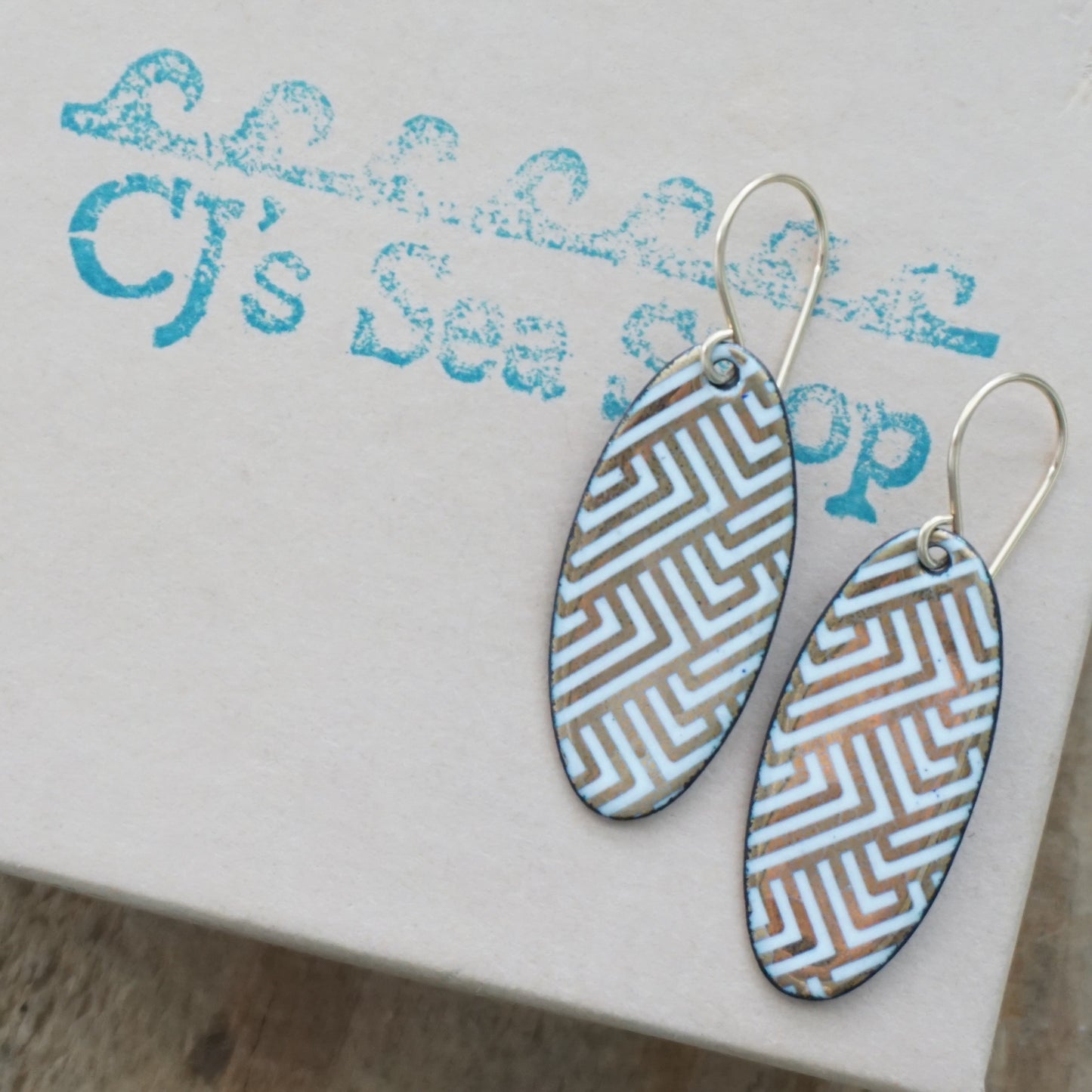 White, oval shaped earrings with gold accents, on a gift box
