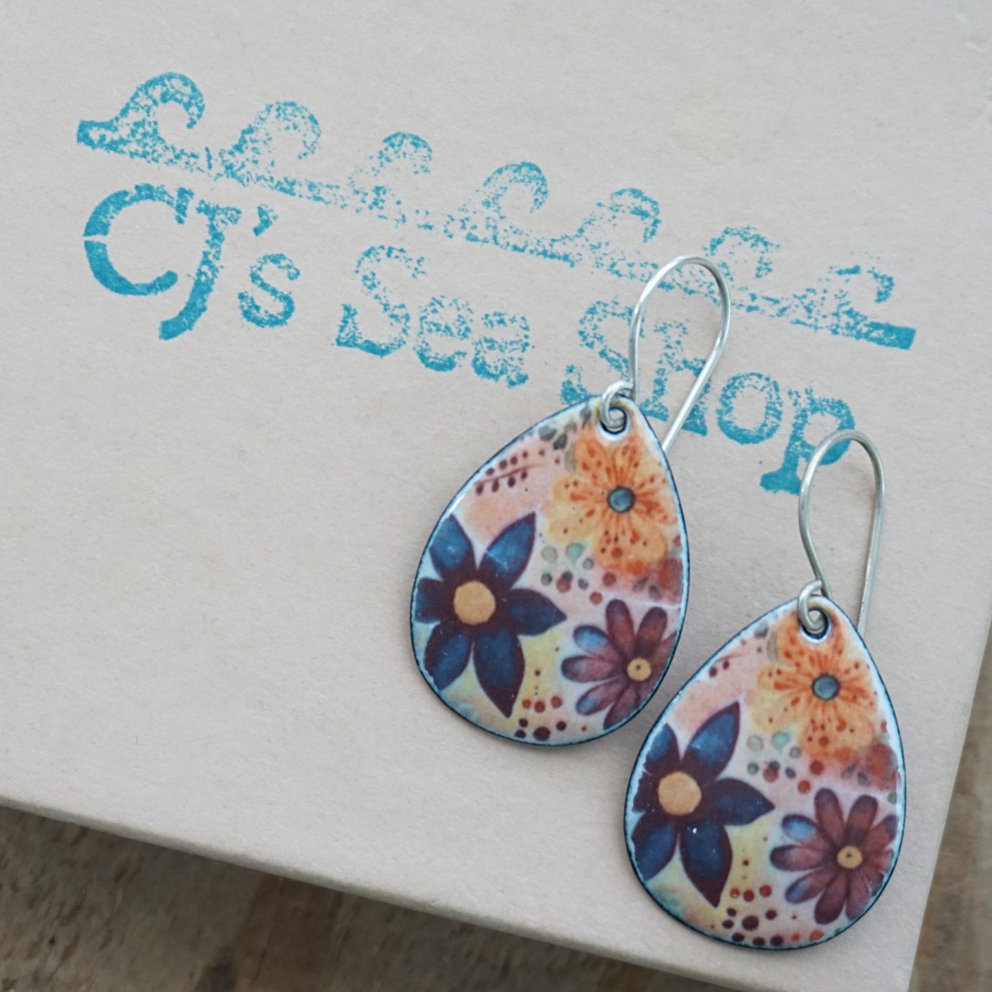 Teardrop-shaped dangle earrings with a colorful floral pattern, displayed on a gift box