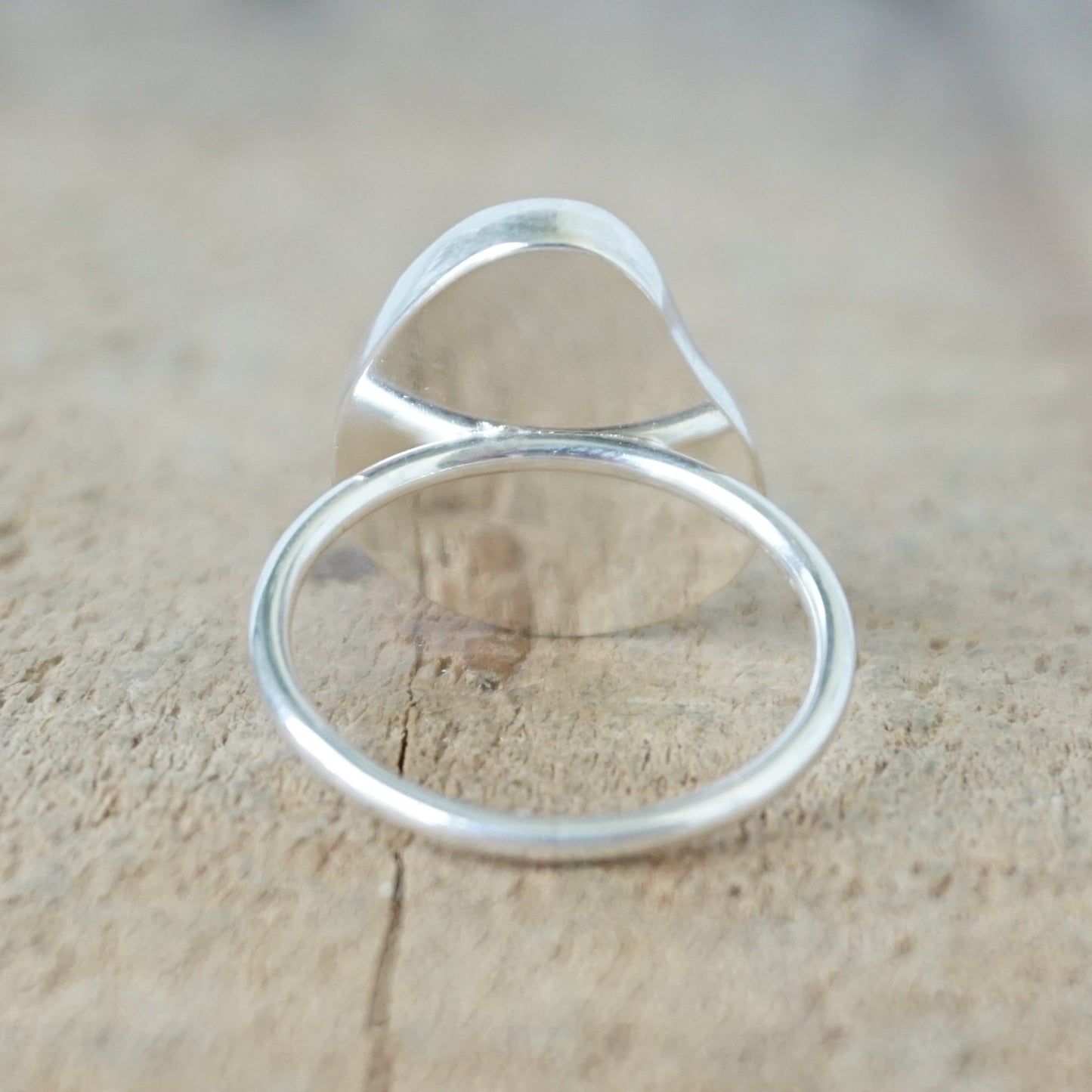 back view of a silver ring with frosted clear sea glass, on a wooden surface.
