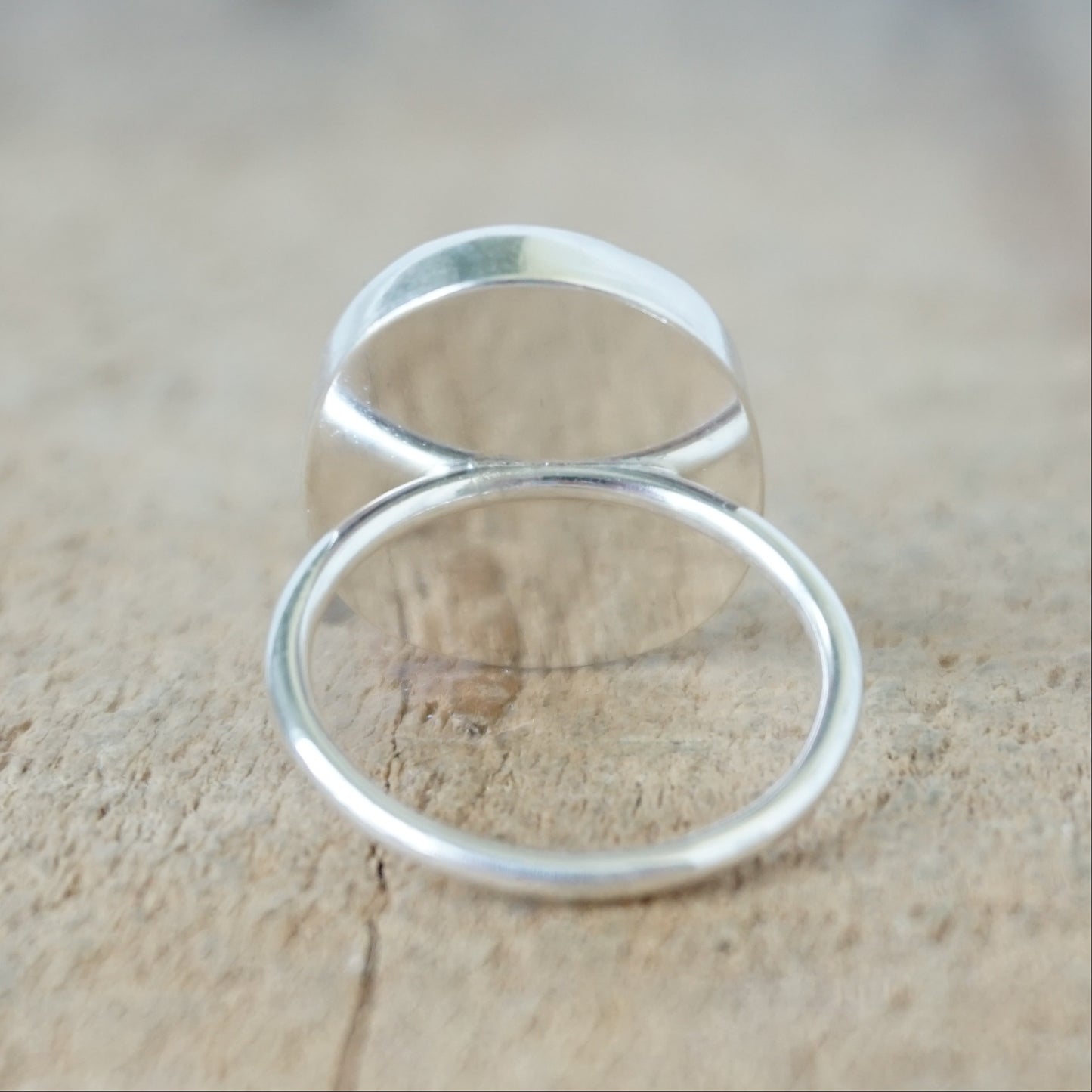 back view of a silver ring with frosted clear sea glass, on a wooden surface.