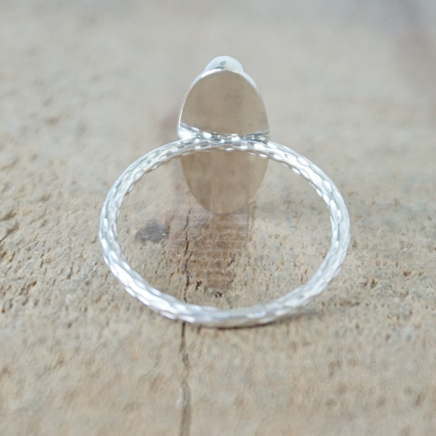 back view of A silver ring with an oval white cabochon gemstone, set on a textured silver band, on a wooden surface.