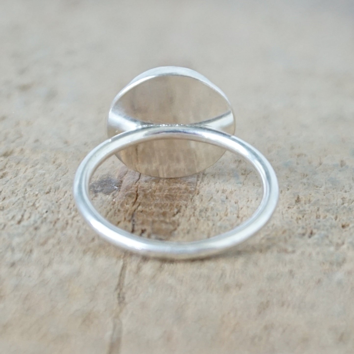 back view of A sterling silver ring featuring a round turquoise cabochon stone with natural dark veining, set against a neutral, textured beige background.