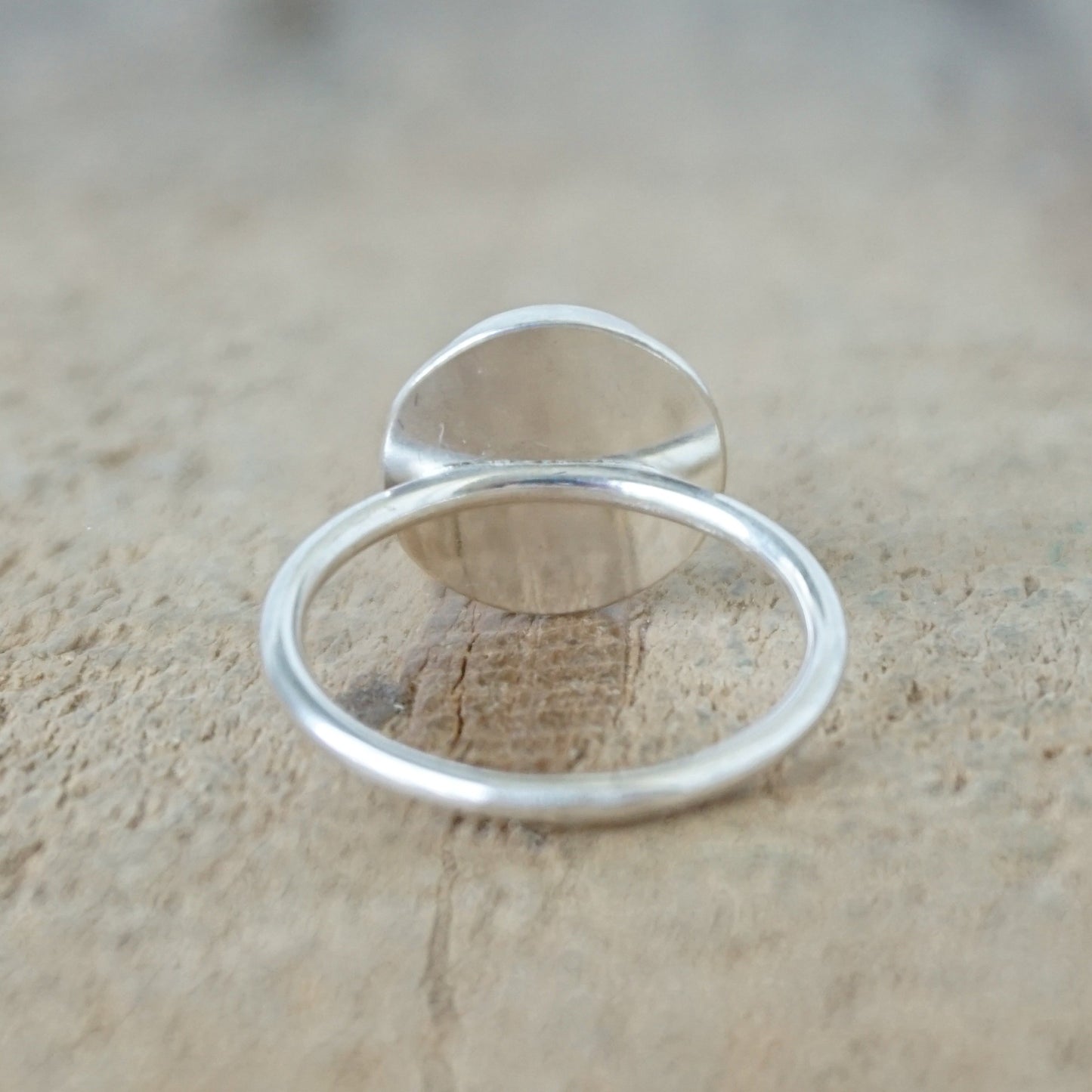 back view of A sterling silver ring featuring a round bezel-set blue lapis lazuli stone with visible golden pyrite inclusions, resting on a textured beige surface.