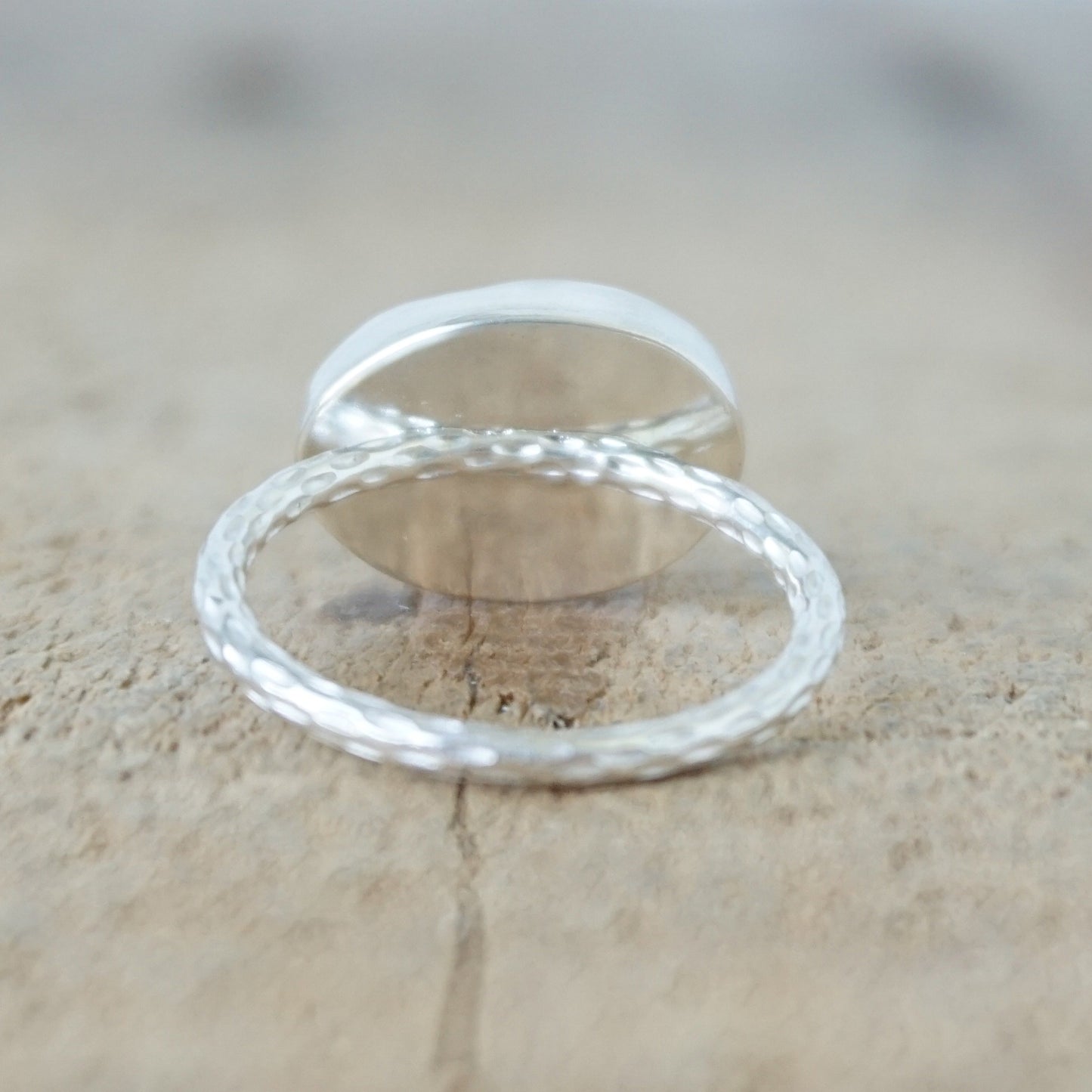 back view of An oval cabochon ring featuring a polished stone with intricate brown, black, and beige banding patterns, set in a silver metal band on a wooden background.