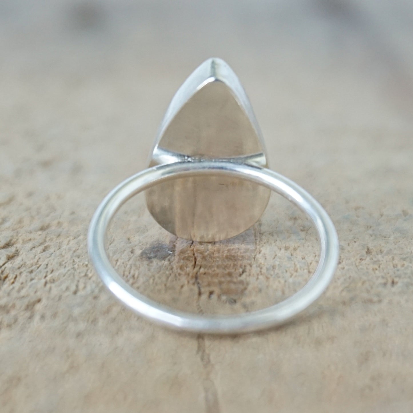 back view of A silver ring featuring a teardrop-shaped gemstone with a white and black marbled pattern, on a wooden surface.
