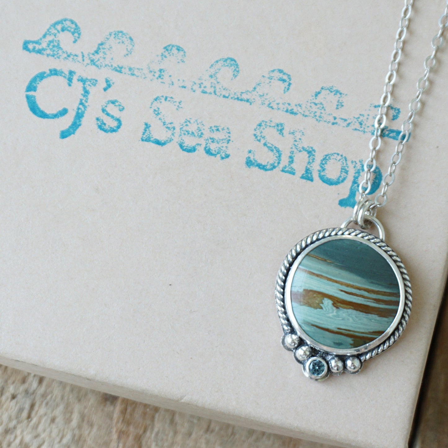 Sterling silver pendant with green and brown stone, displayed on a gift box