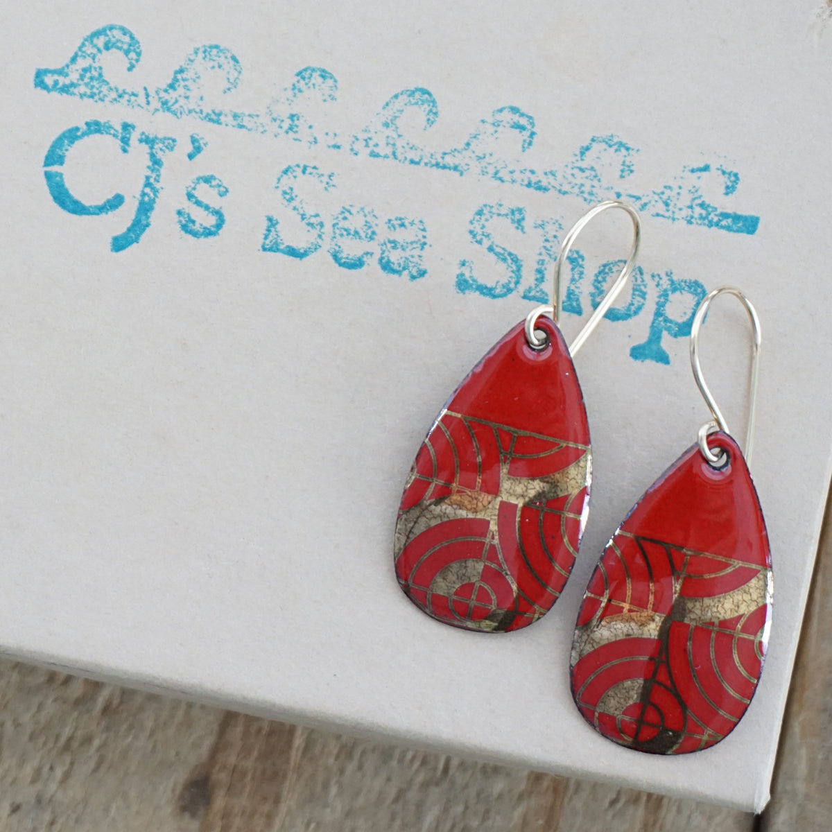 Teardrop shaped red enamel earrings with gold geometric design, displayed on a gift box