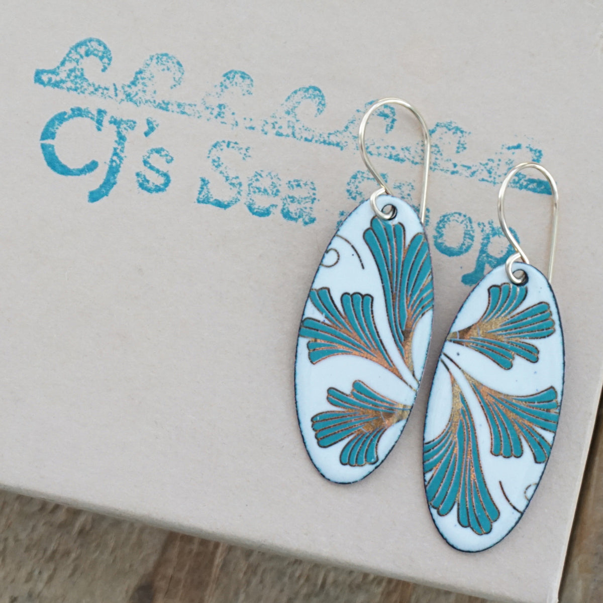 Oval shaped enamel earrings with green and gold leaves, displayed on a gift box
