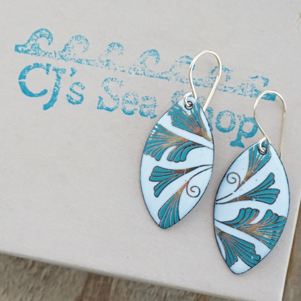 Marquis shaped enamel earrings with green and gold leaves, displayed on a gift box