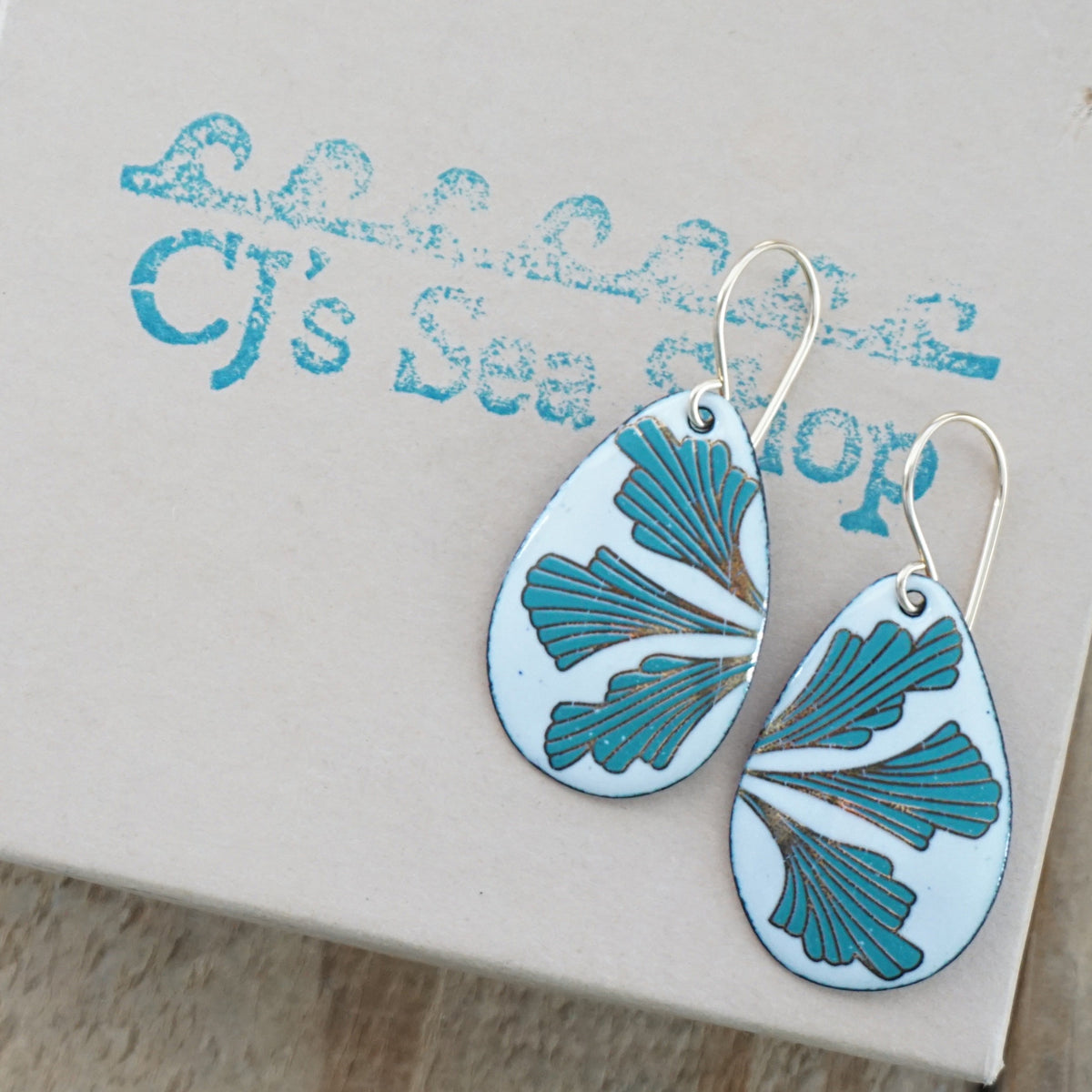 Teardrop shaped enamel earrings with green and gold leaves, displayed on a gift box