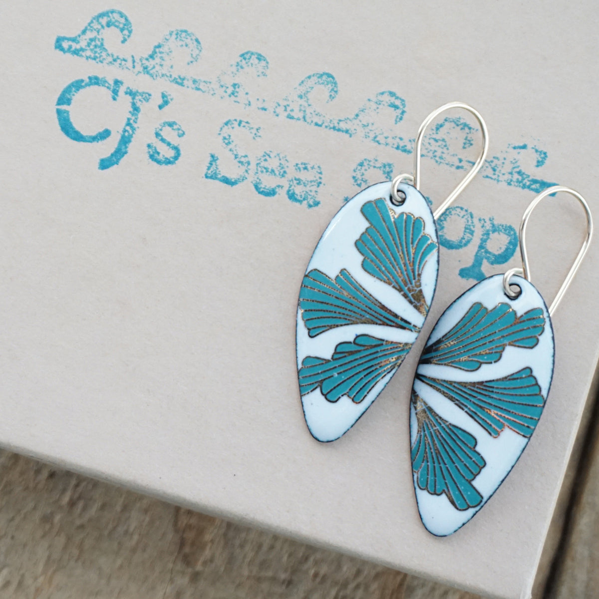 Teardrop shaped enamel earrings with green and gold leaves, displayed on a gift box