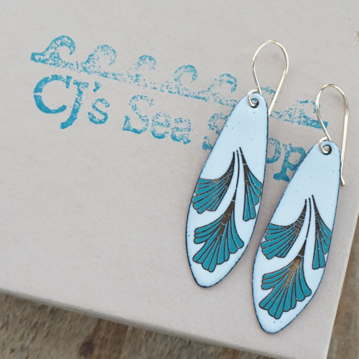 Teardrop shaped enamel earrings with green and gold leaves, displayed on a gift box