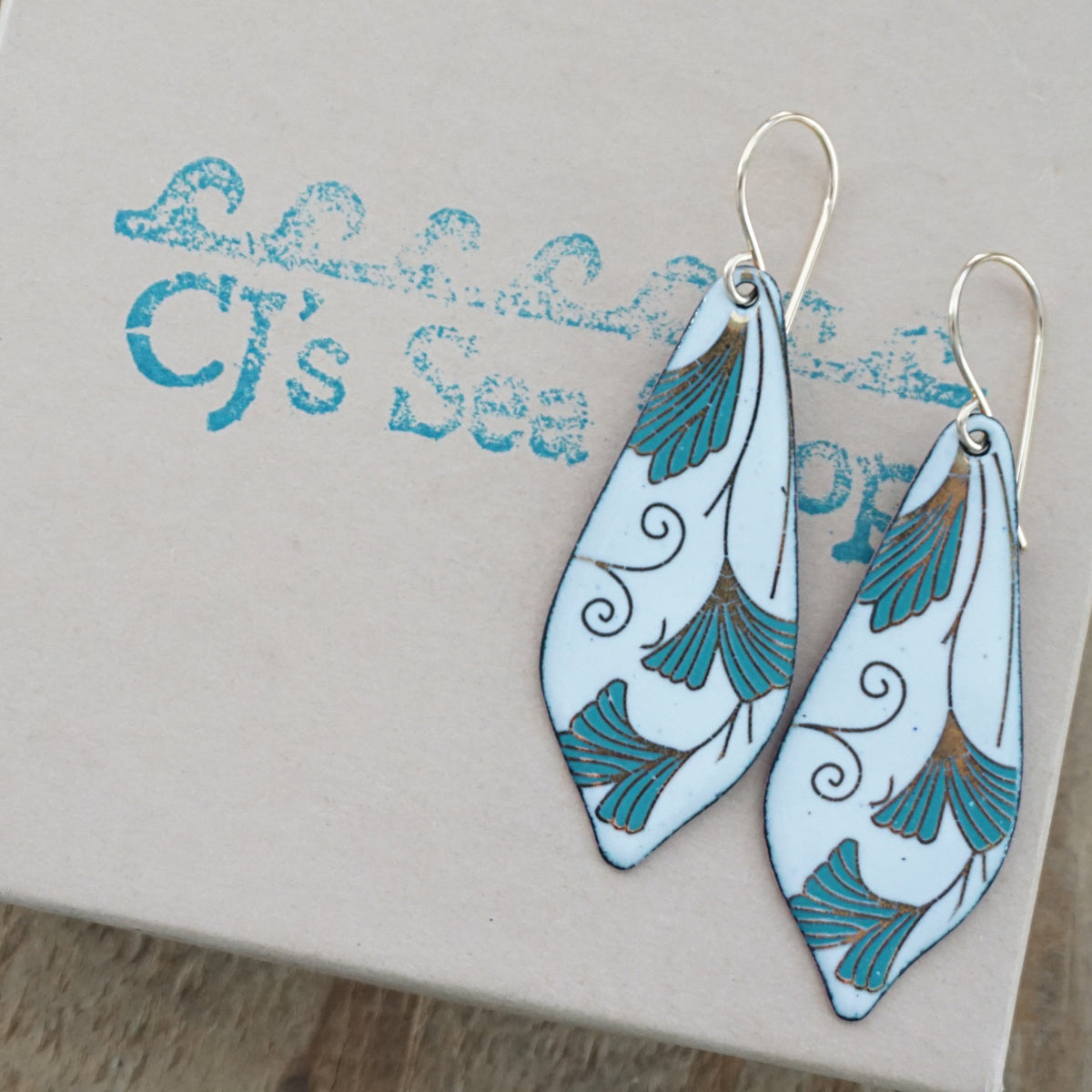 Teardrop shaped enamel earrings with green and gold leaves, displayed on a gift box