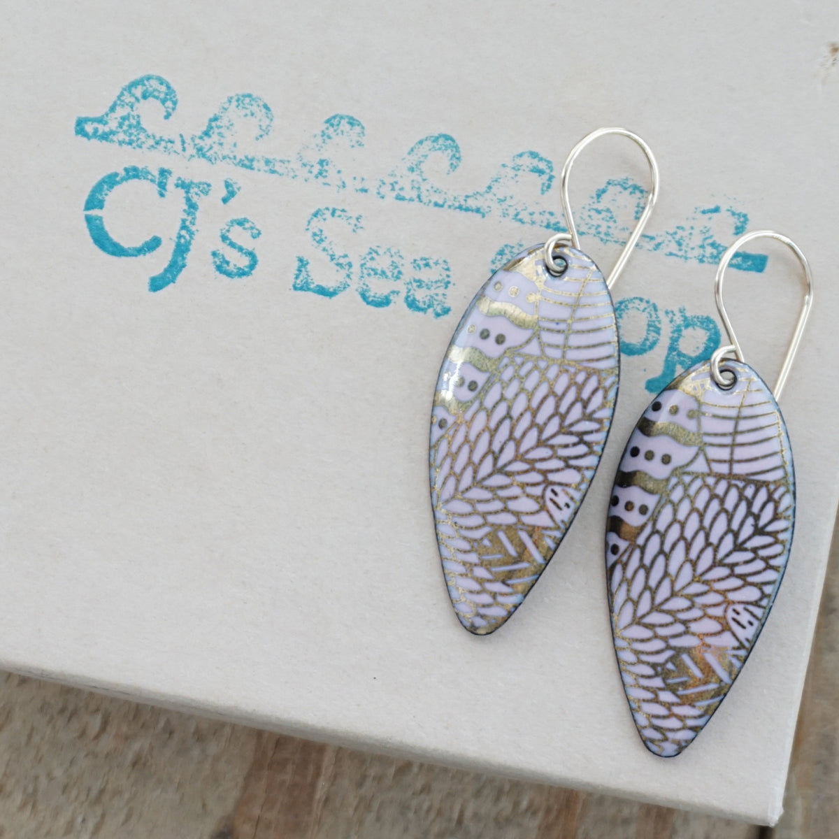 a pair of pink enamel earrings with gold designs, displayed on a gift box