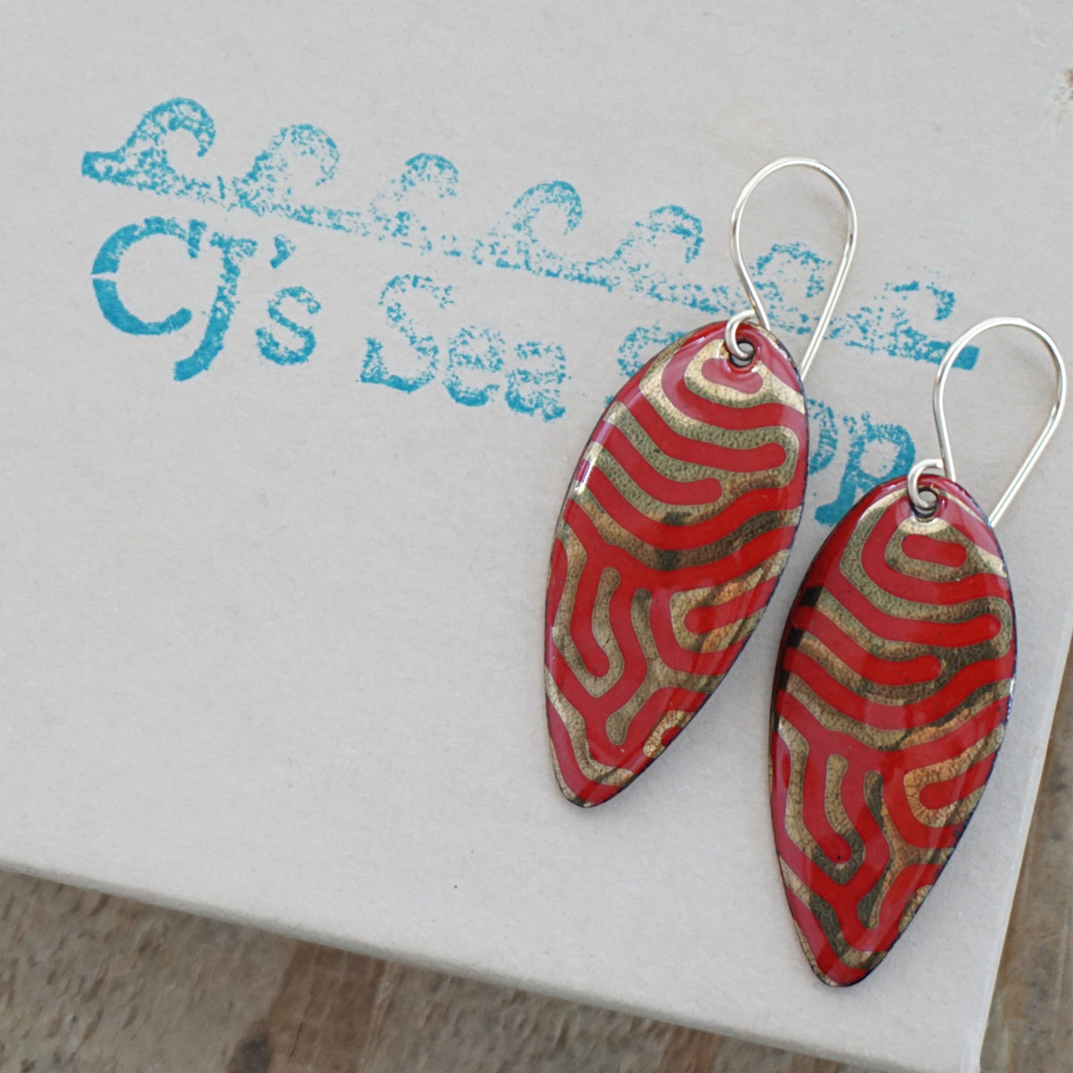 a pair of red enamel earrings with gold designs, displayed on a gift box