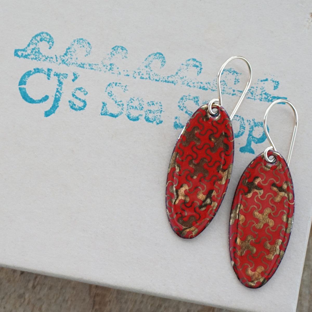 a pair of red enamel earrings with gold designs, displayed on a gift box