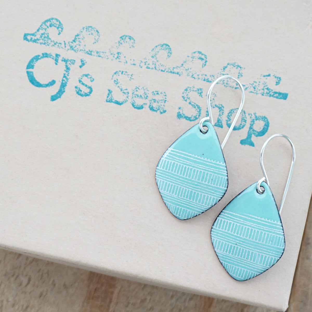 a pair of green enamel kite shaped earrings with white line accents, displayed on a gift box