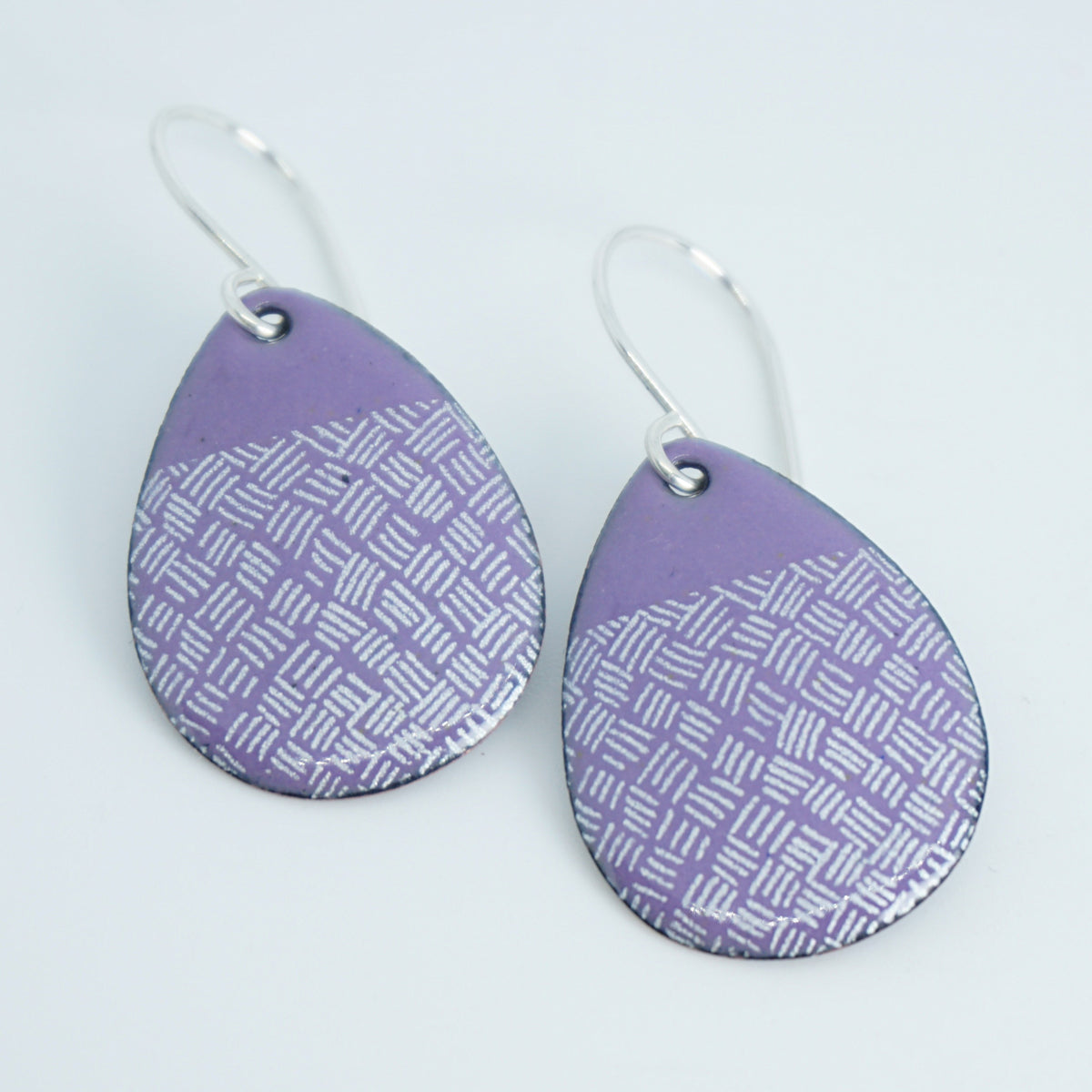 a pair of purple enamel teardrop shaped earrings with white line accents, against a white background