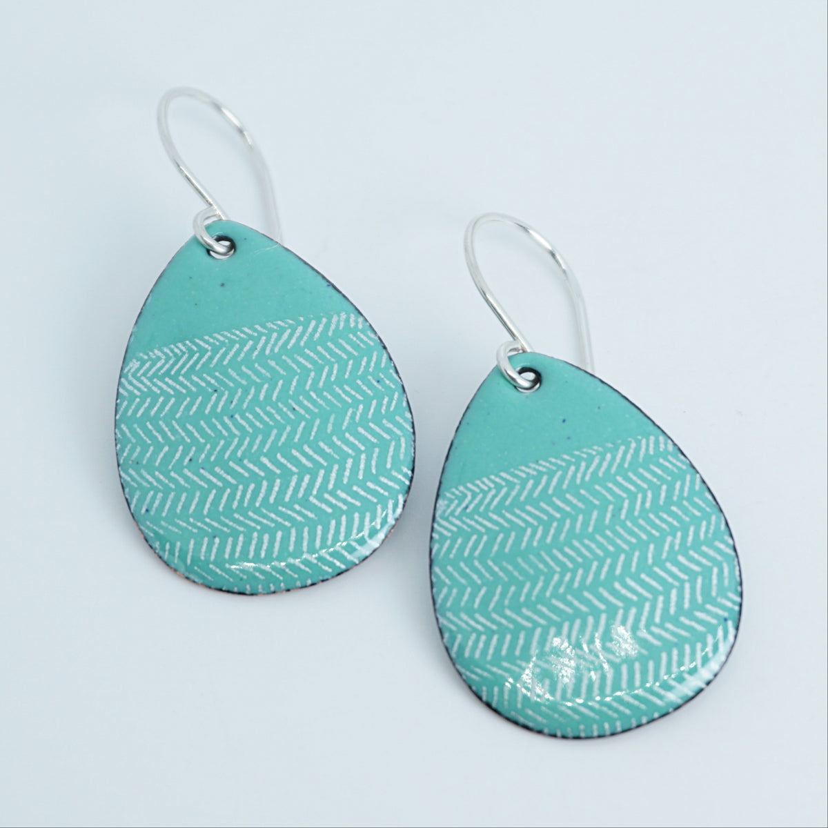 a pair of green enamel teardrop shaped earrings with white line accents, against a white background