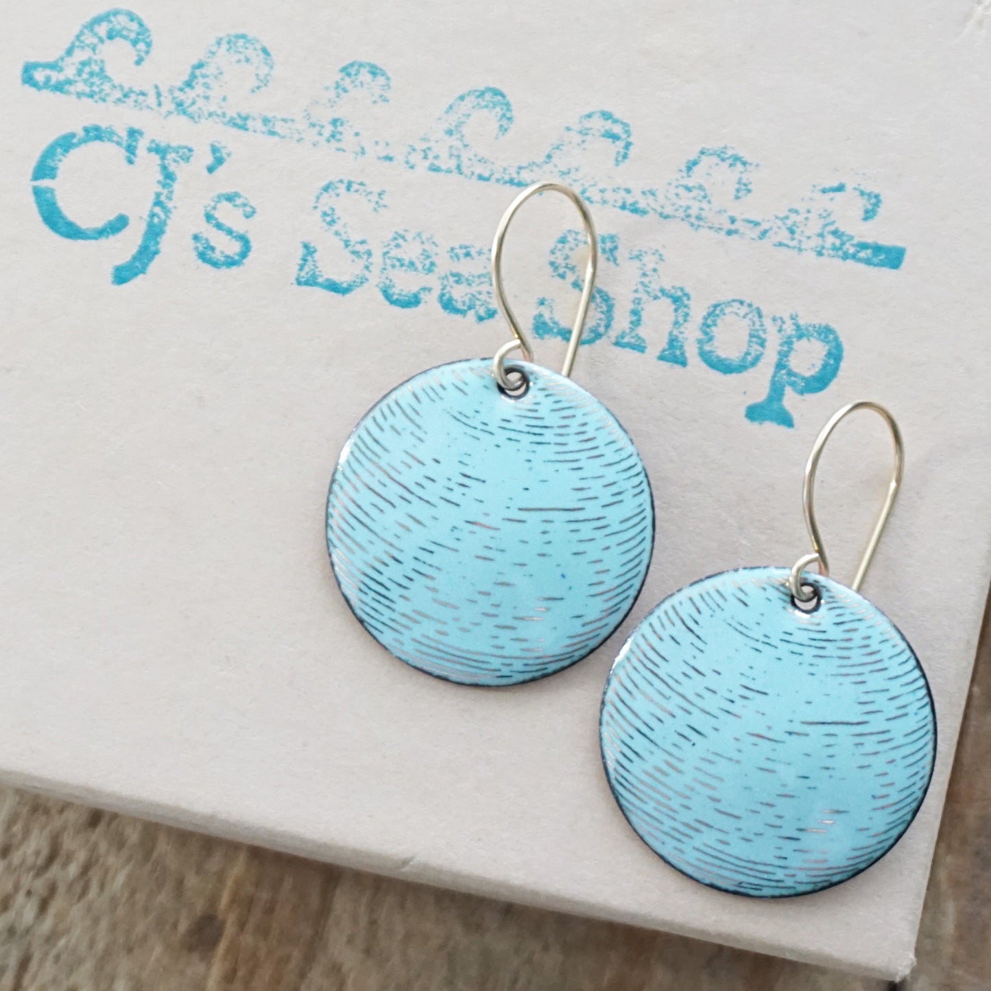A pair of blue enamel disc earrings with gold accents on a gift box
