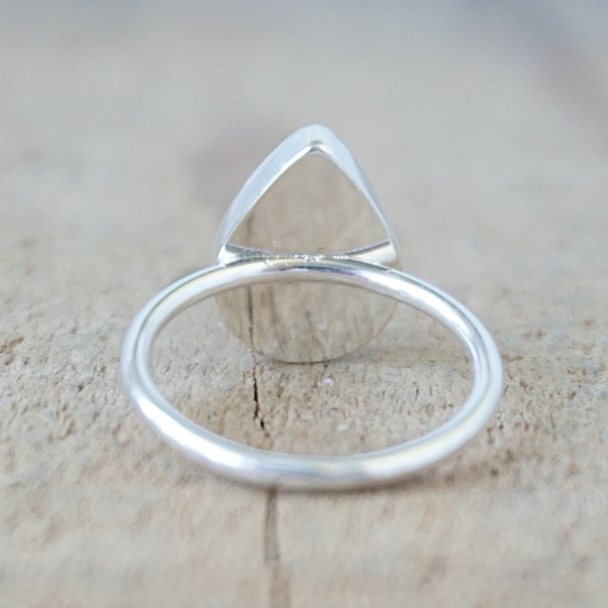 back view of a silver ring with a white and dark grey stone, against a wooden background