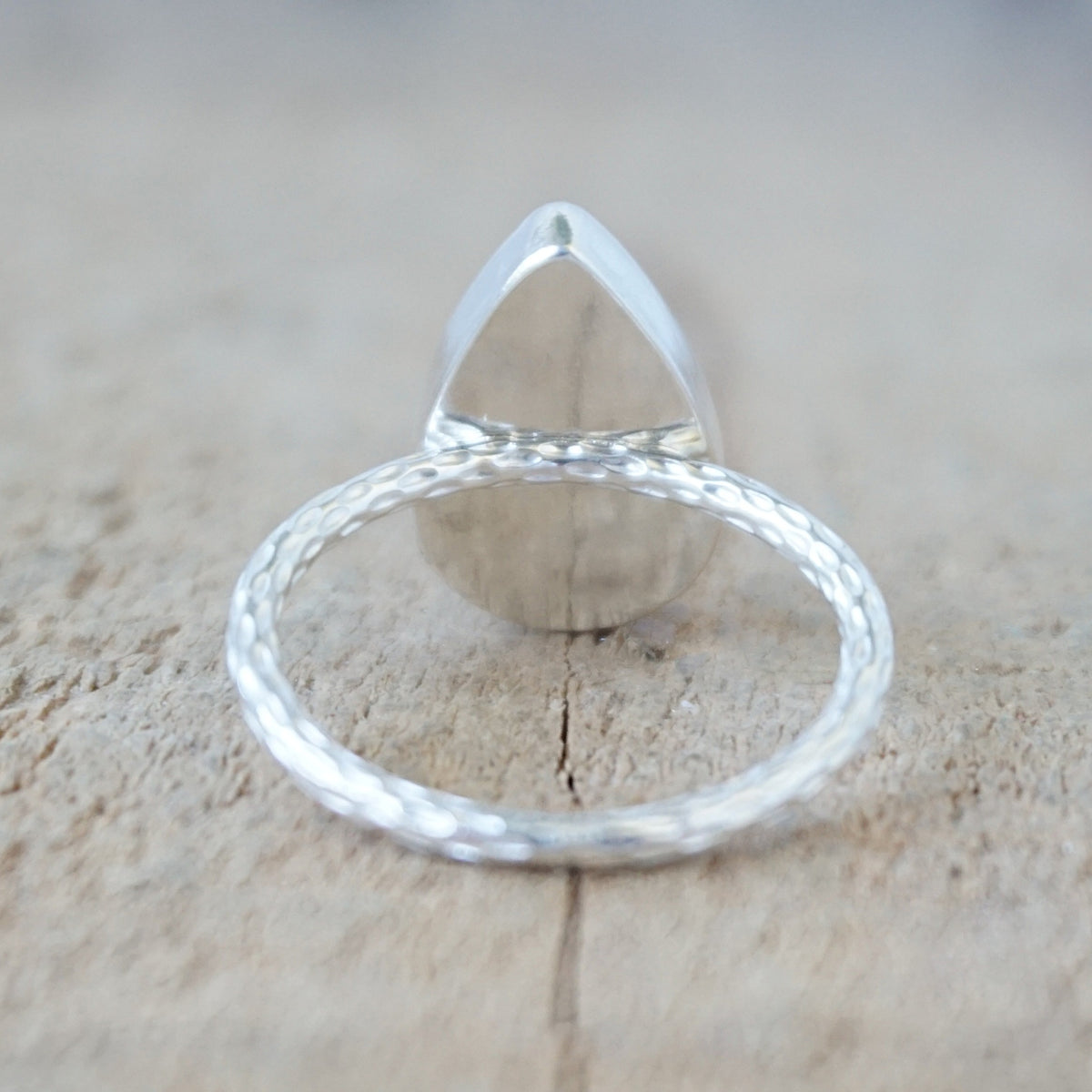 back view of a silver ring with a dark grey stone, against a wooden background