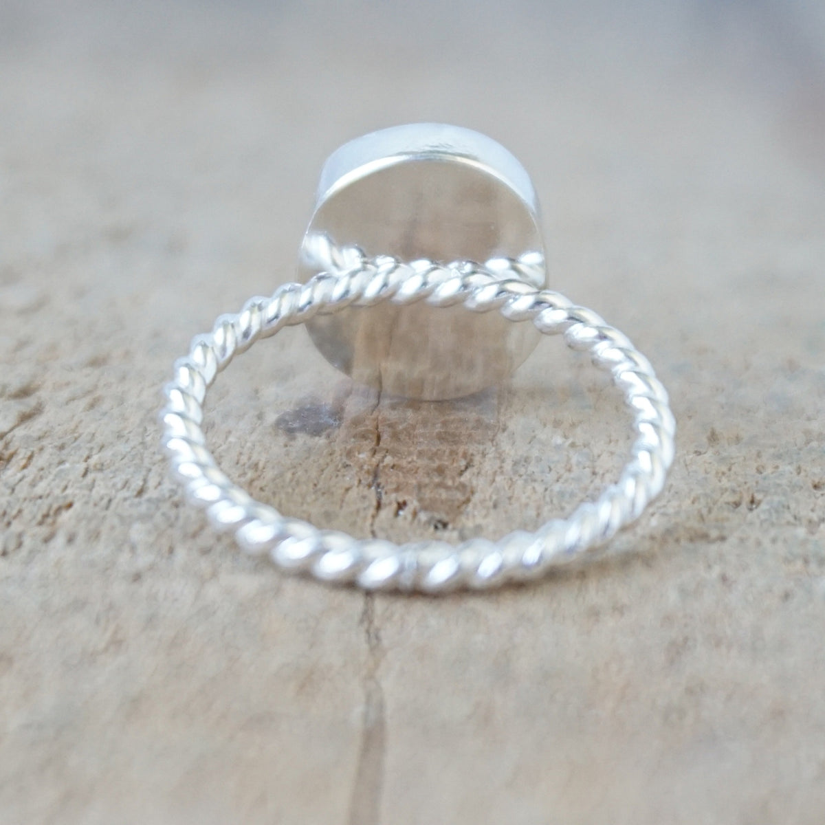 back view of a silver ring with a piece of green sea glass, against a wooden background