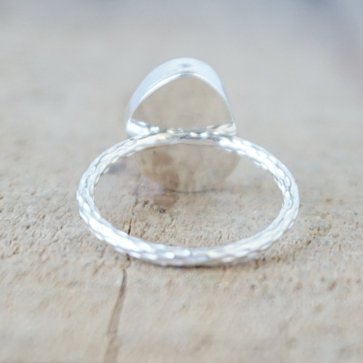 back view of a silver ring with a piece of green sea glass, against a wooden background