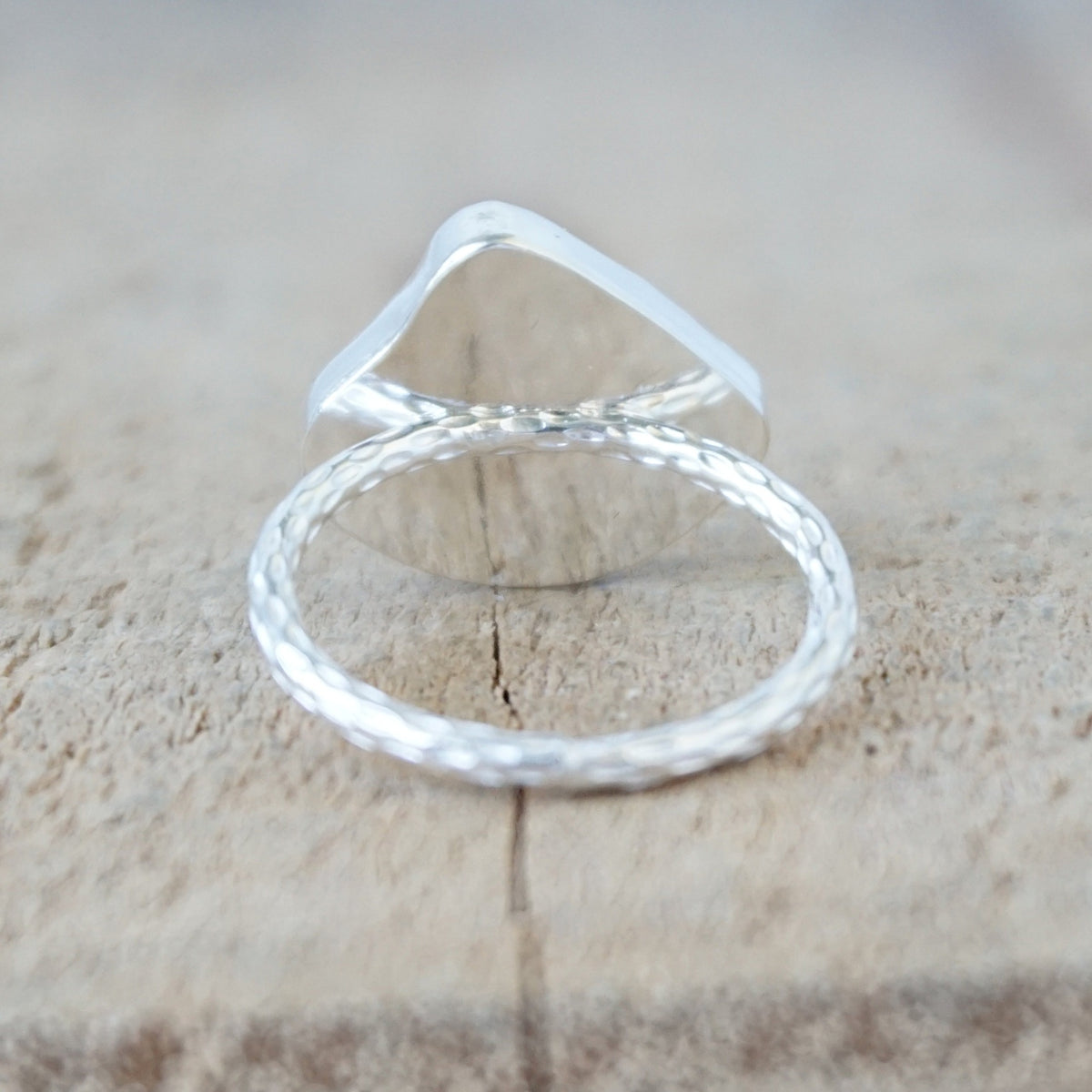 back view of a silver ring with a piece of teal blue sea glass, against a wooden background