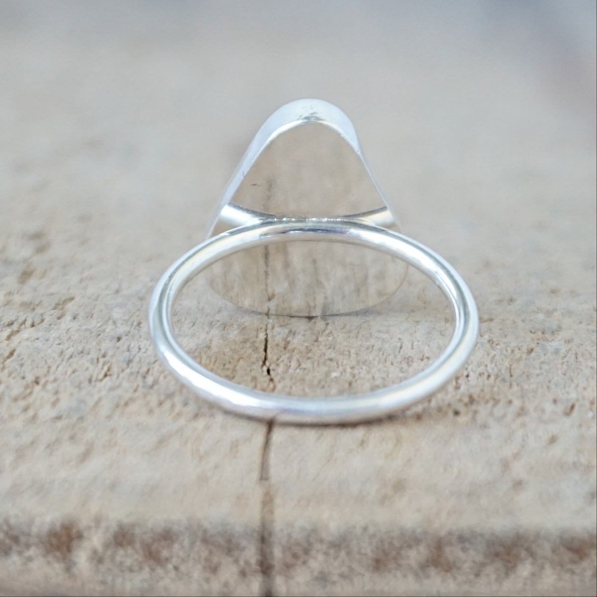 back view of a silver ring with a piece of teal blue sea glass, against a wooden background