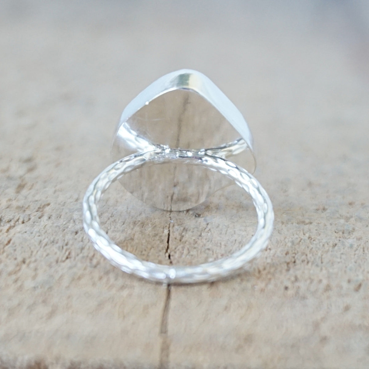 back view of a silver ring with a piece of seafoam green sea glass, against a wooden background