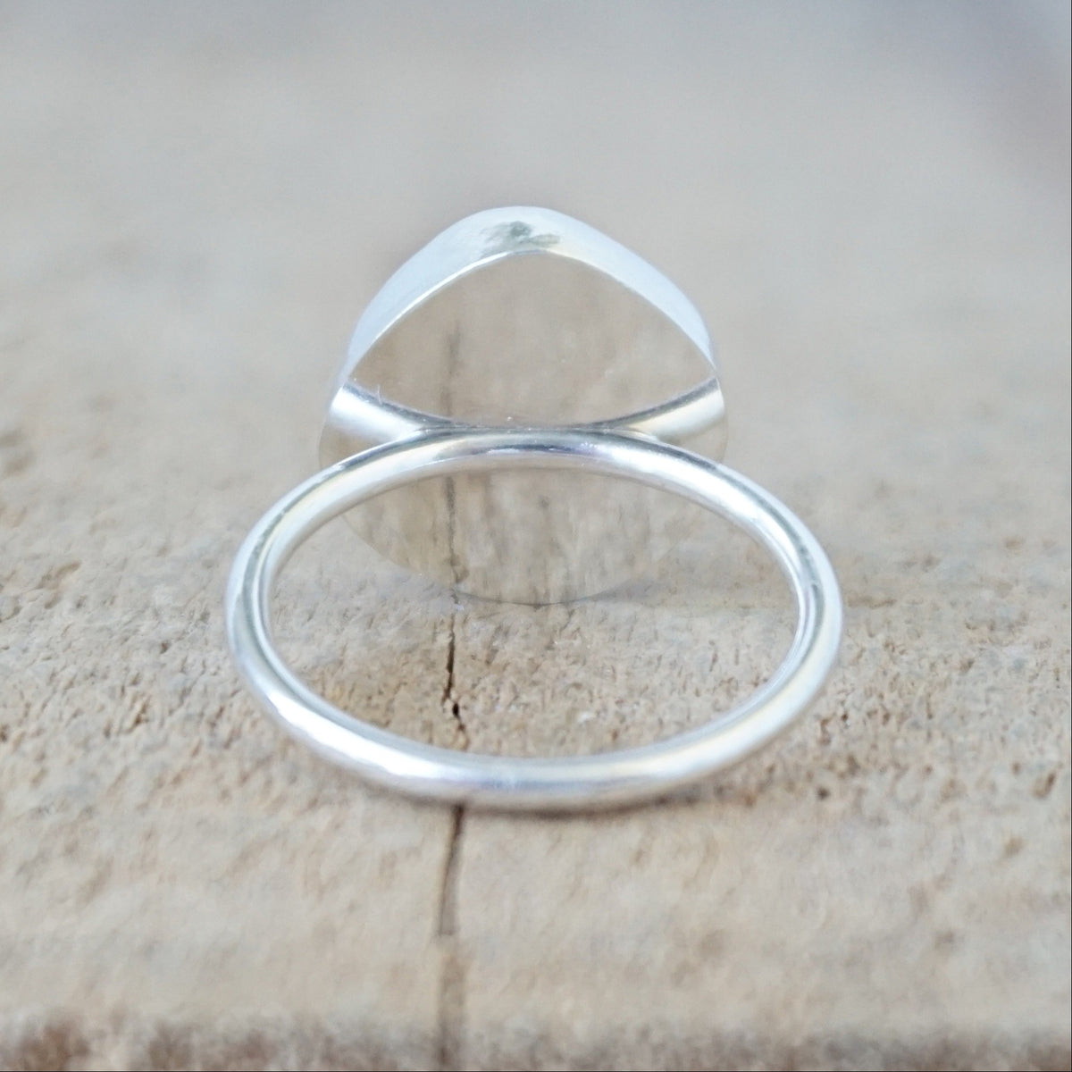 back view of a silver ring with a piece of teal blue sea glass, against a wooden background