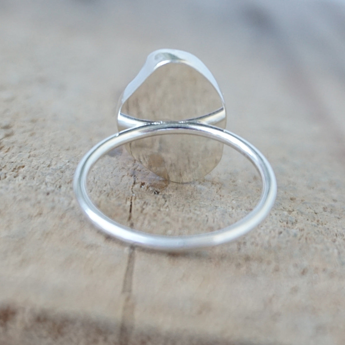 back view of a silver ring with a piece of light blue sea glass, against a wooden background