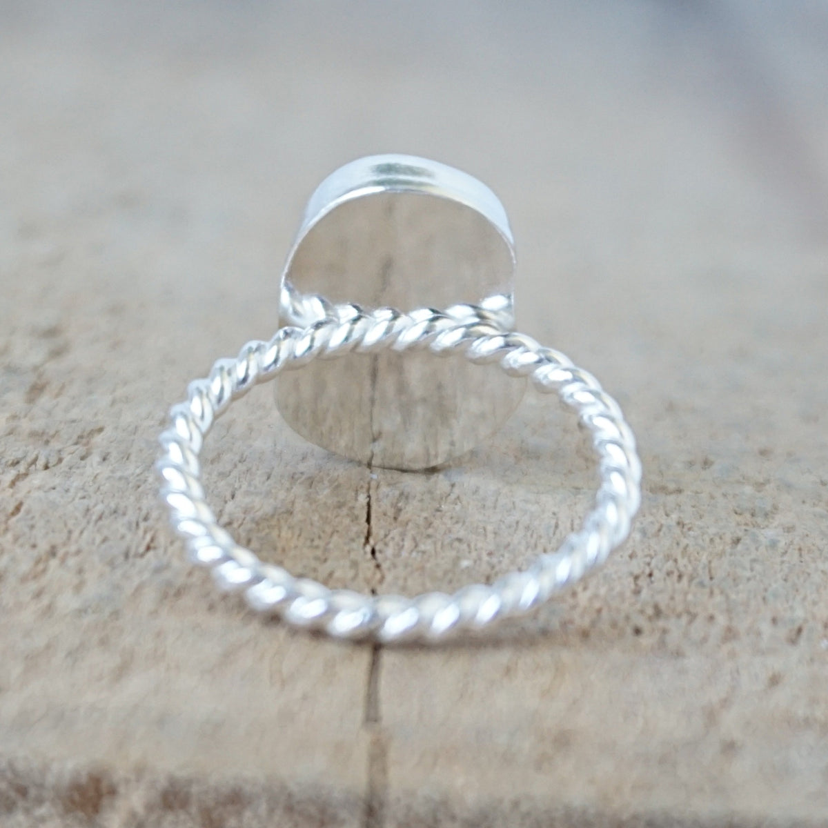 back view of a silver ring with a piece of light blue sea glass, against a wooden background