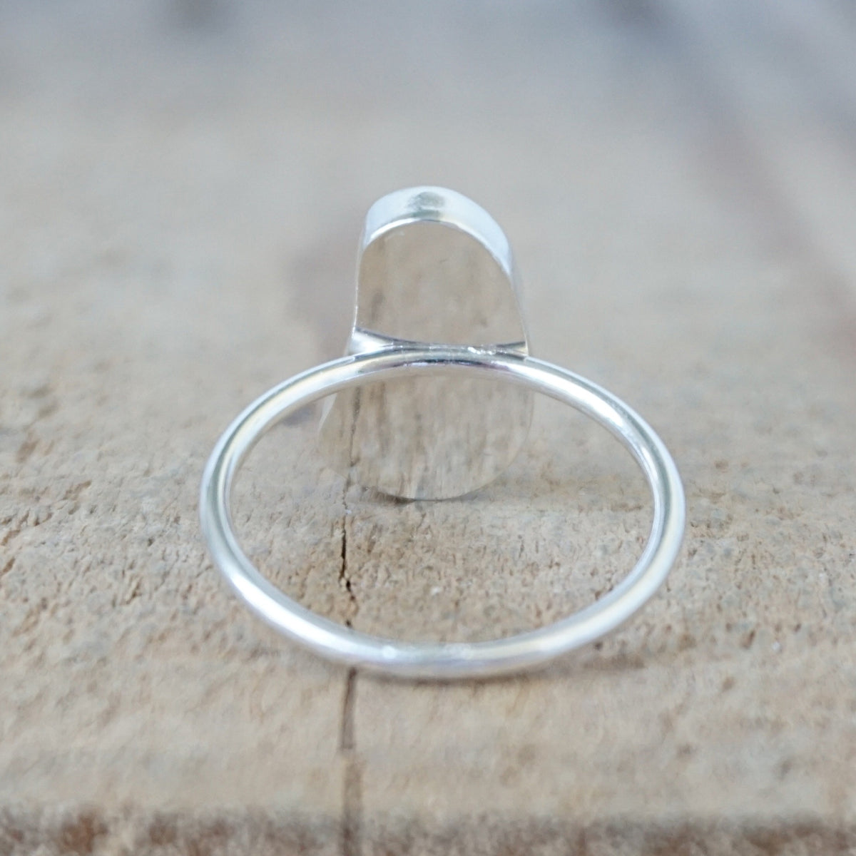 back view of a silver ring with a piece of light blue sea glass, against a wooden background