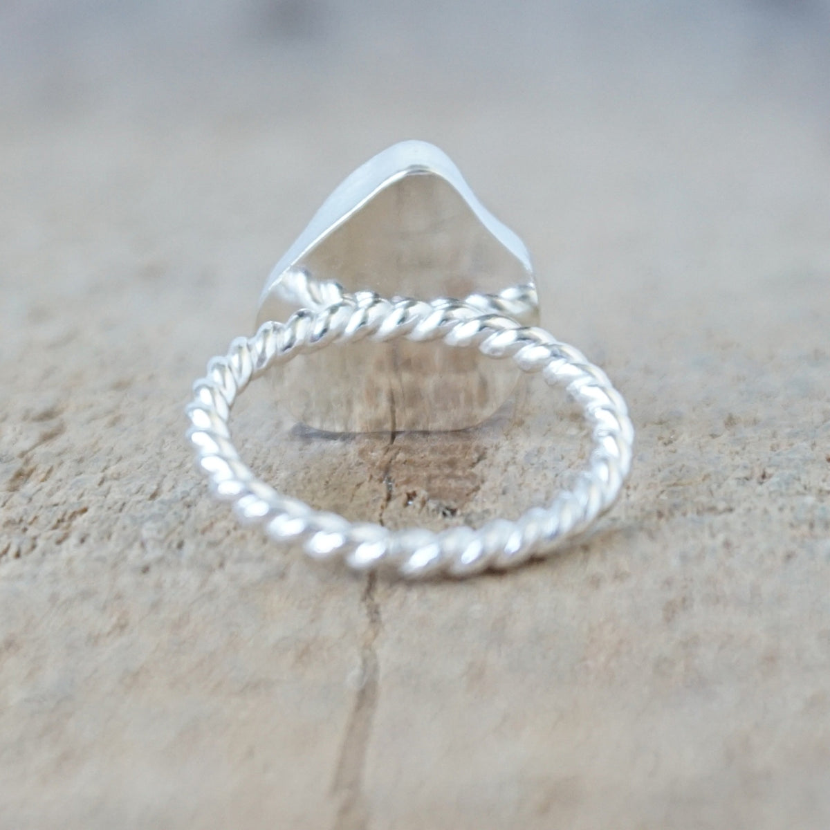 back view of a silver ring with a piece of light blue sea glass, against a wooden background