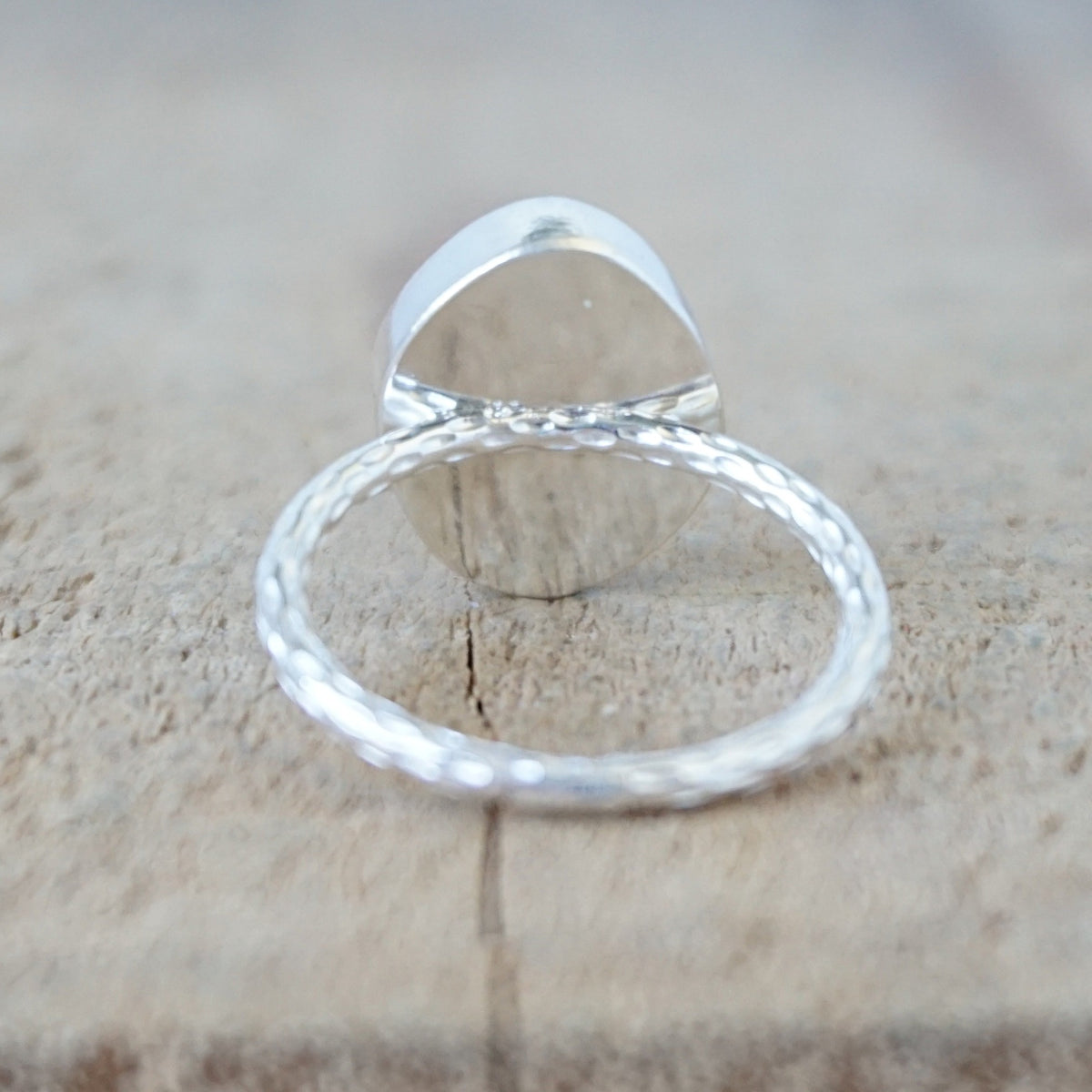 back view of a silver ring with a piece of light blue sea glass, against a wooden background