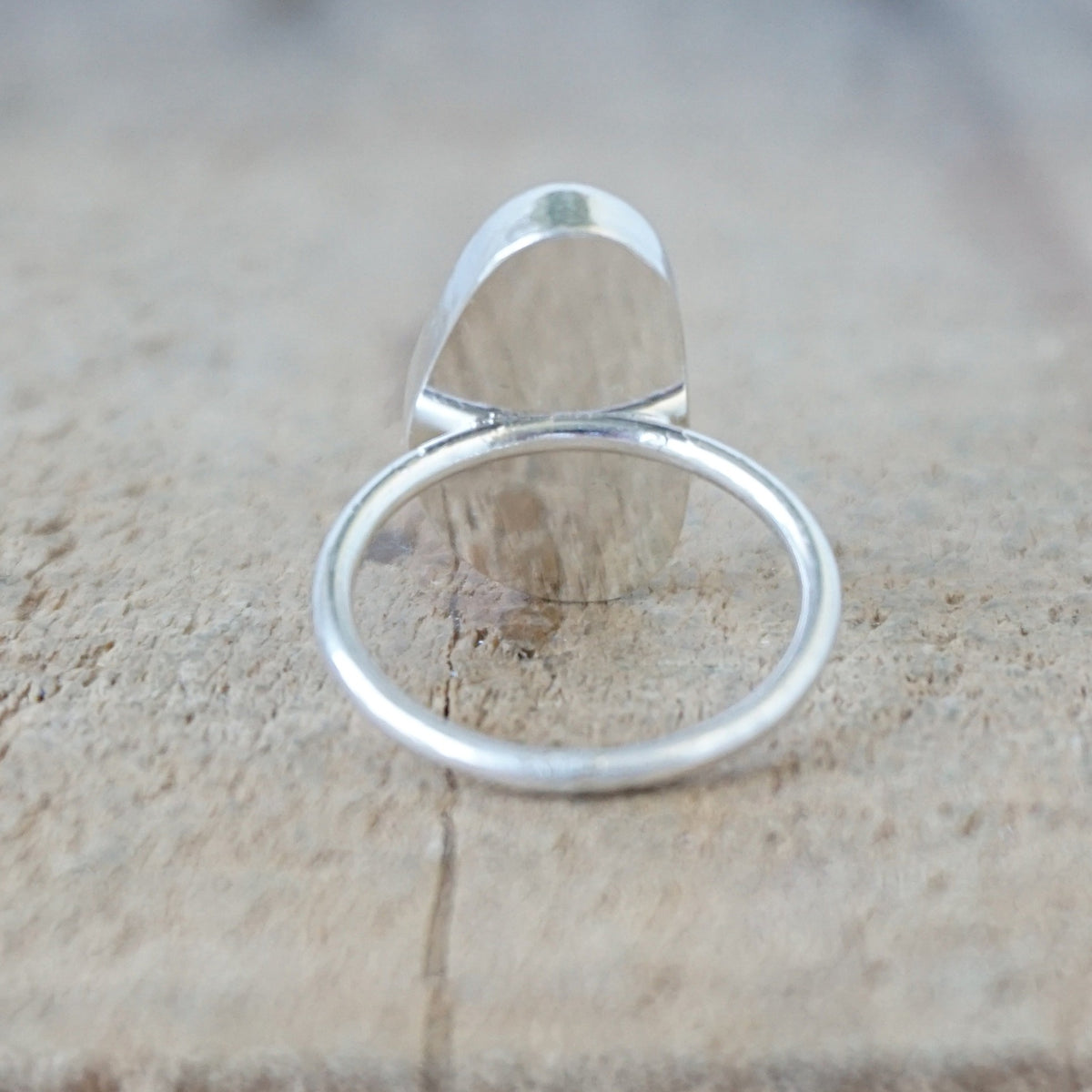 back view of a silver ring with a piece of pale lavender sea glass, against a wooden background