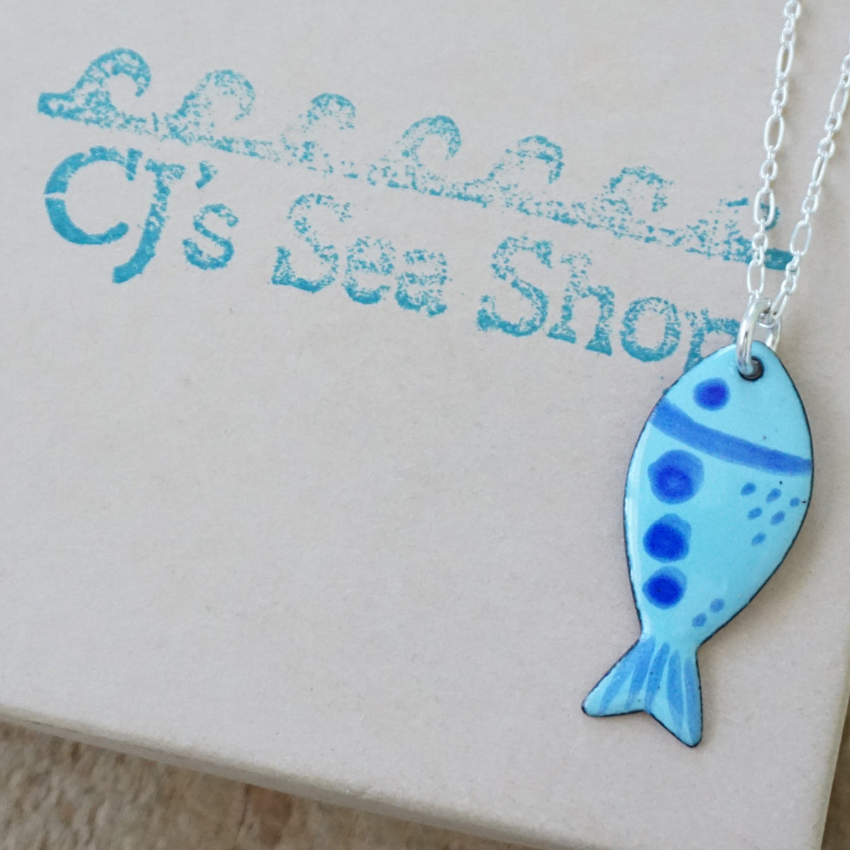 blue enamel fish shaped pendant, displayed on a gift box