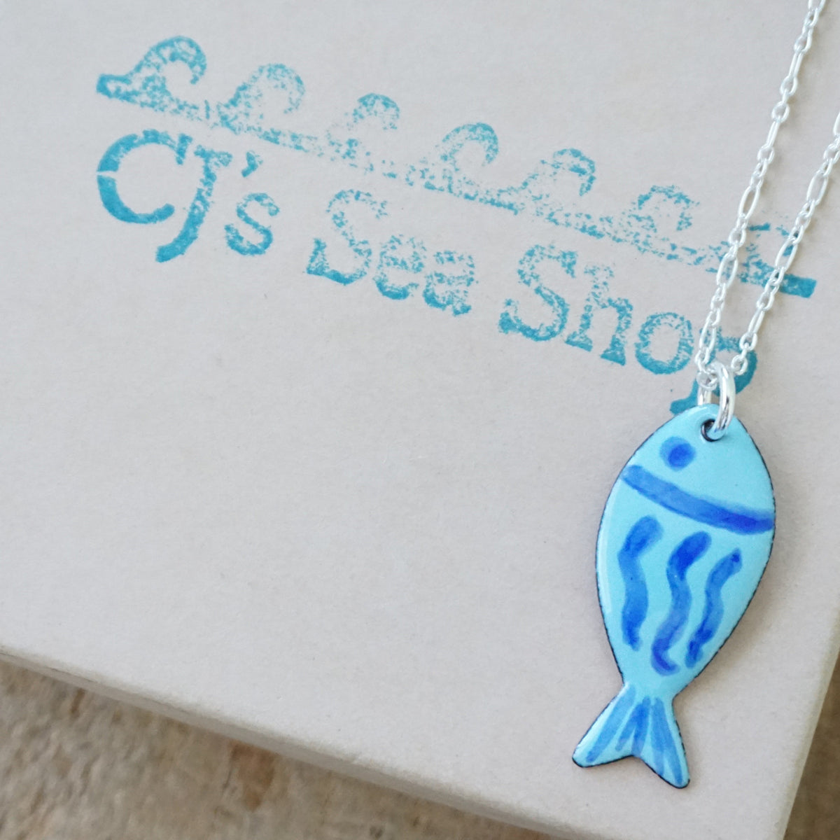 blue enamel fish shaped pendant, displayed on a gift box