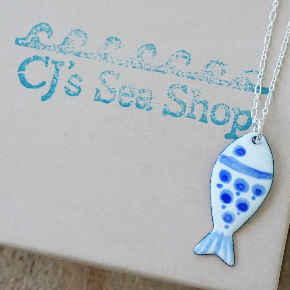 white and blue enamel fish shaped pendant, displayed on a gift box
