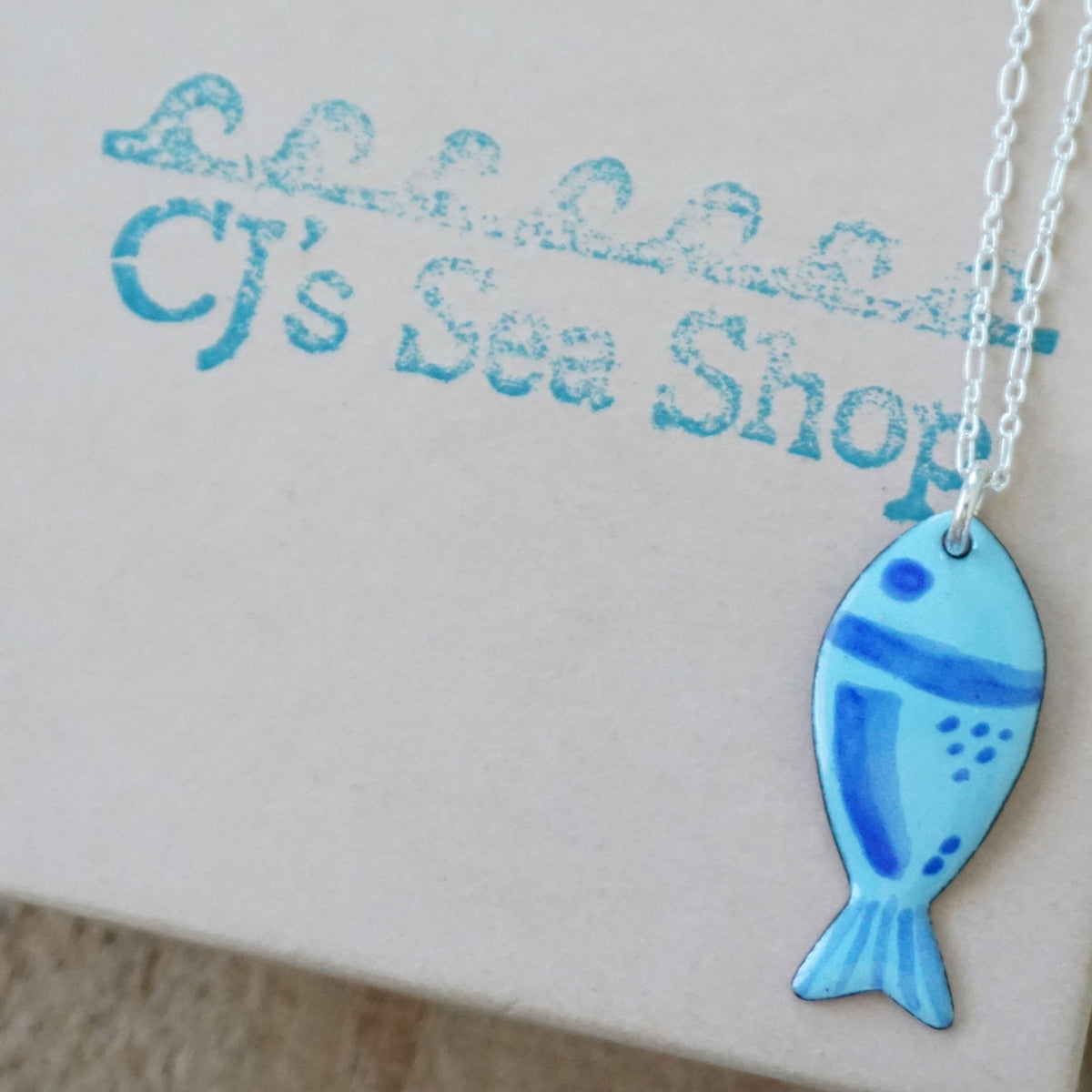 blue enamel fish shaped pendant, displayed on a gift box