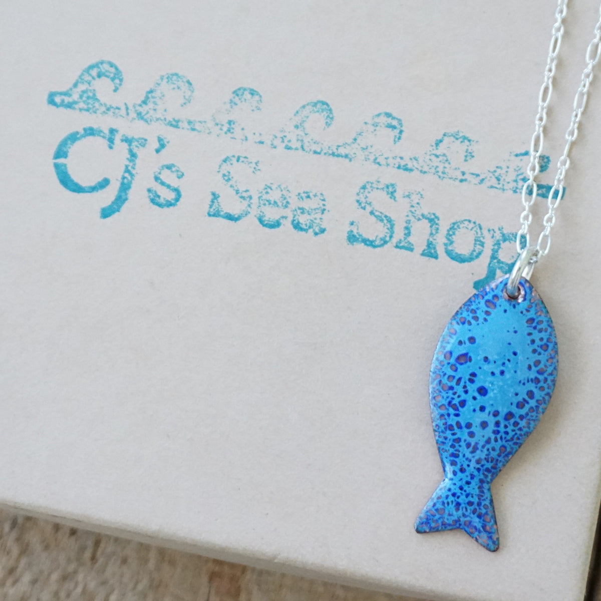 Blue enamel fish shaped pendant displayed on a gift box