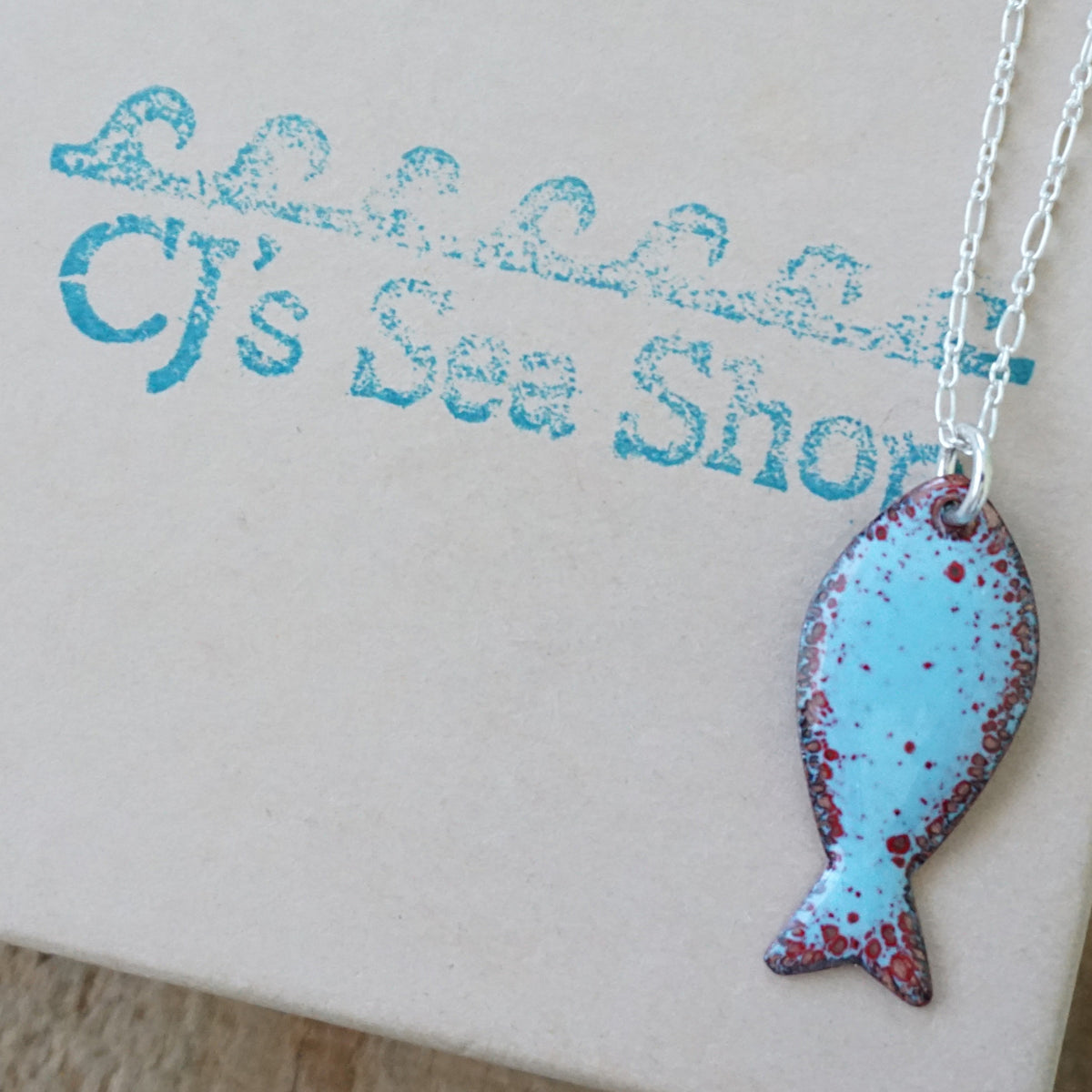 light blue and red enamel fish shaped pendant displayed on a gift box
