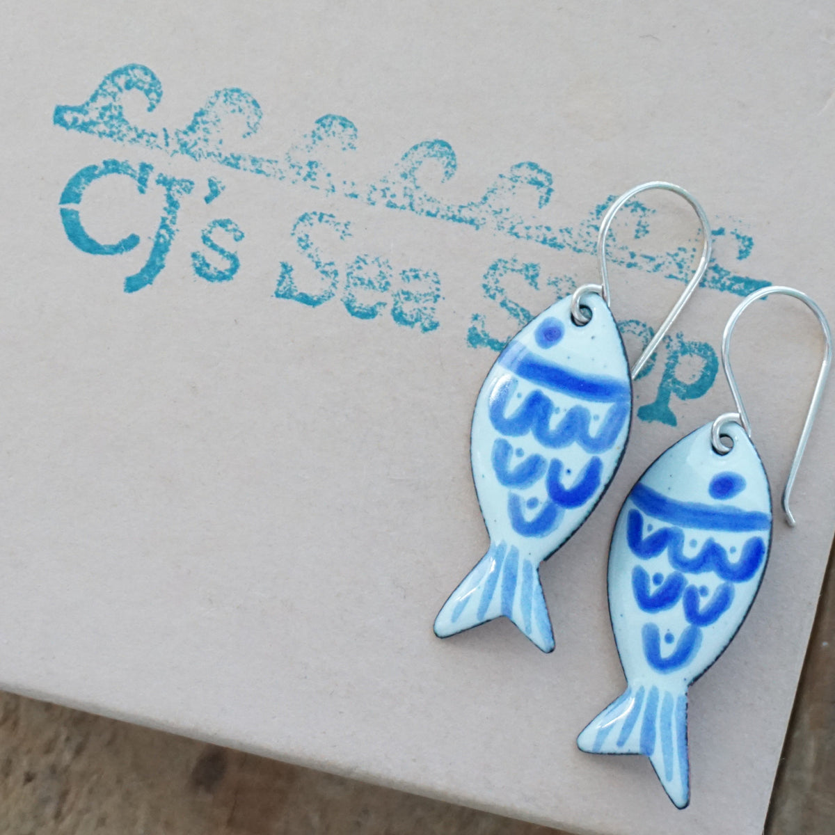 light green and blue enamel fish shaped earrings, displayed on a gift box