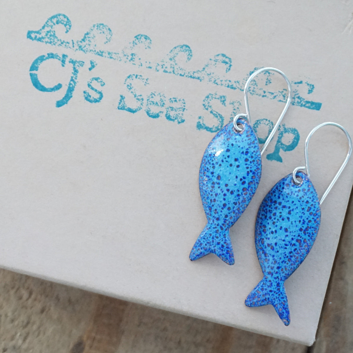 blue enamel fish shaped earrings, displayed on a gift box