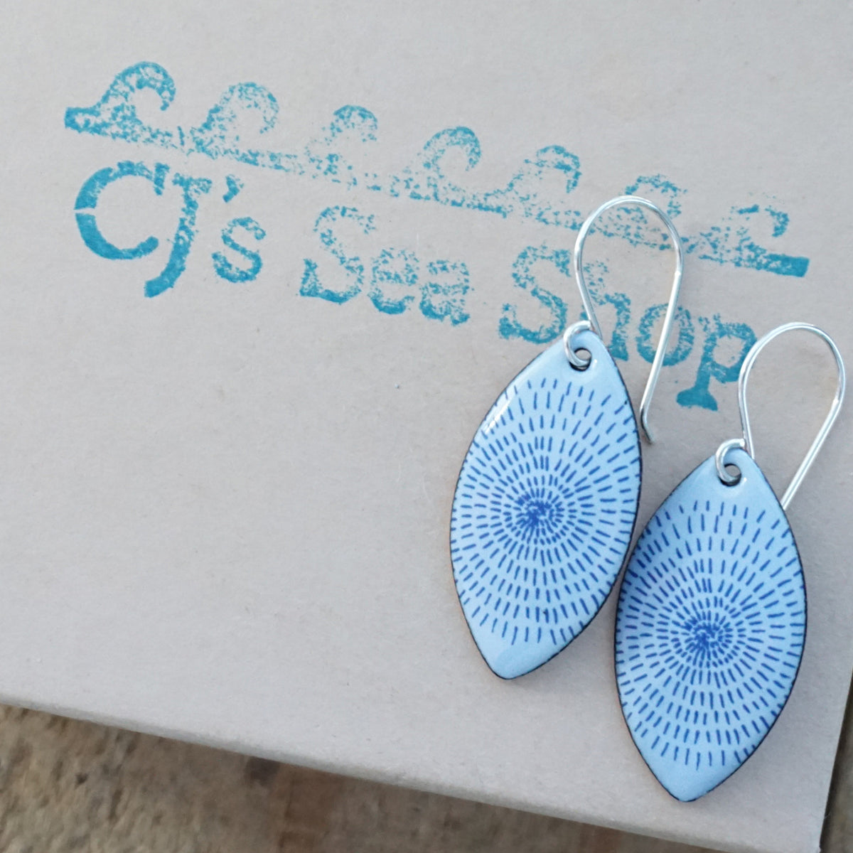 a pair of light purple enamel marquis shaped earrings with blue accents, displayed on a gift box