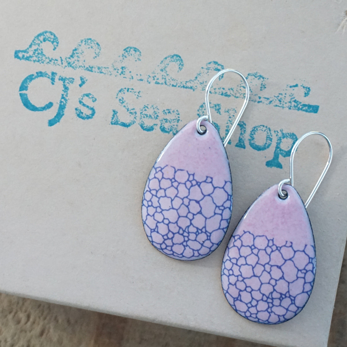 a pair of pink enamel teardrop shaped earrings with blue bubble accents, displayed on a gift box